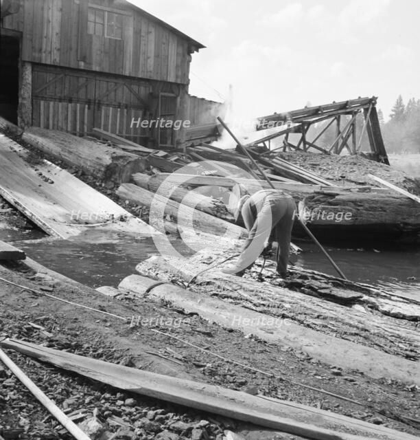 Pond monkey steers log raft in mill pond, Keno, Klamath County, Oregon, 1939. Creator: Dorothea Lange.