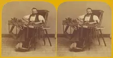 Portrait of Charles H. Barnes, Hardwick, Mass. seated in handicapped-style chair making ..., 1870s. Creator: George T Putnam