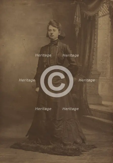Portrait of a young woman in long black dress, standing, about 1900. Creator: George W Killian.