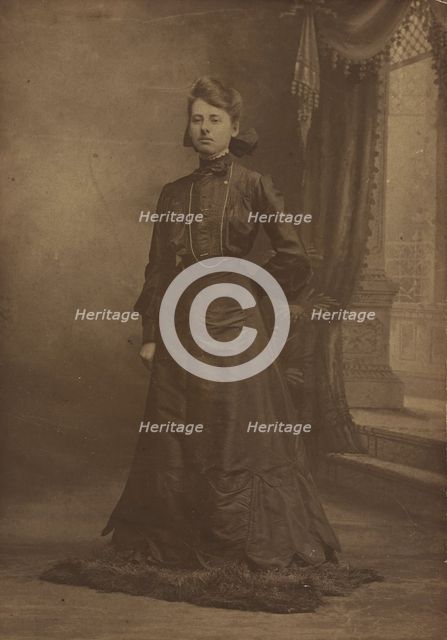 Portrait of a young woman in long black dress, standing, about 1900. Creator: George W Killian.