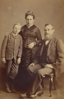 Portrait of an unidentified family: mother and son standing, bearded father seated, 1865-1875. Creator: John McKean
