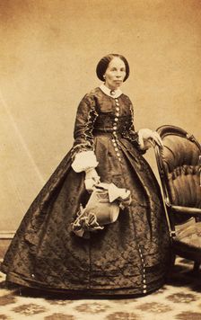 Portrait of older woman, standing, holding bonnet, c1860. Creator: CK Bill