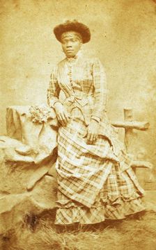 Portrait of unidentified young woman in plaid dress and hat, c1880-c1889. Creator: Thomas Gates