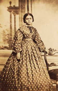 Portrait of young woman wearing patterned dress, with bow at neck, c1860. Creator: Coss & Leach