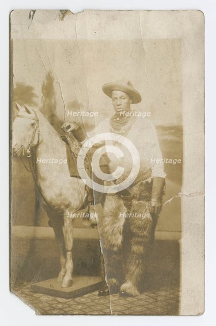 Postcard of a man posing in a Western scene in a photography studio, early 20th century. Creator: Unknown.