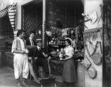 Pan-American Exposition, Buffalo, N.Y., 1901: Man in wheeled chair at souvenir shop with 4..., 1901. Creator: Frances Benjamin Johnston