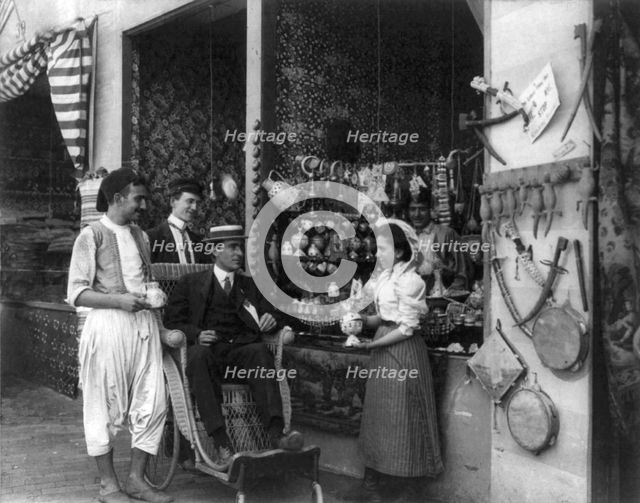Pan-American Exposition, Buffalo, N.Y., 1901: Man in wheeled chair at souvenir shop with 4..., 1901. Creator: Frances Benjamin Johnston.