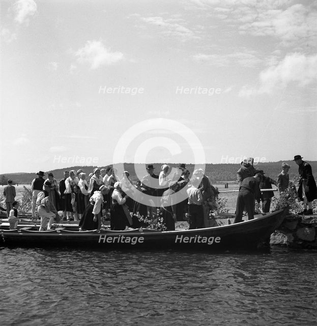 People arrive in long boats, called church boats, Midsummer's Eve and Day celebrations, 1941. Creator: Torkel Lindeberg.