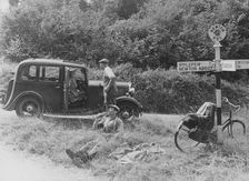 People relaxing by a signpost with a 1935 Standard 10 hp car, Devon, (c1935?)