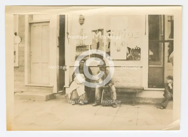 Photograph of a man and woman sitting outside of a storefront, early 20th century. Creator: Unknown.