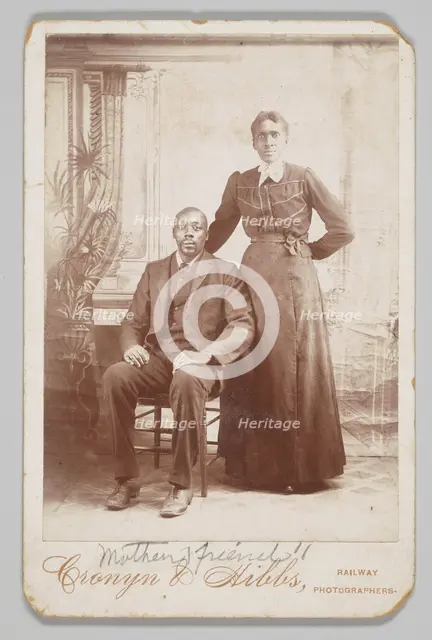 Photograph of a man sitting down with a woman standing next to him, 1880s - 1900. Creator: Cronyn & Hibbs.
