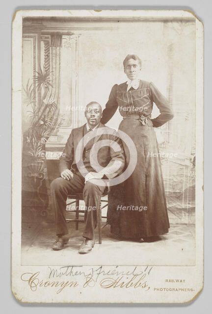 Photograph of a man sitting down with a woman standing next to him, 1880s - 1900. Creator: Cronyn & Hibbs.