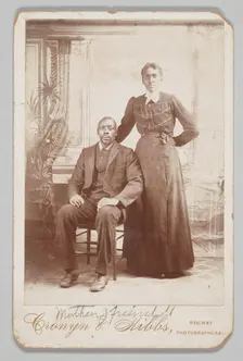 Photograph of a man sitting down with a woman standing next to him, 1880s - 1900. Creator: Cronyn & Hibbs
