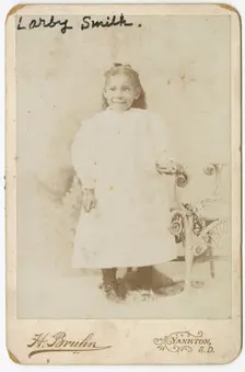 Photograph of Larby Smith standing next to a wicker chair., late 19th century. Creator: Henry Bruhn