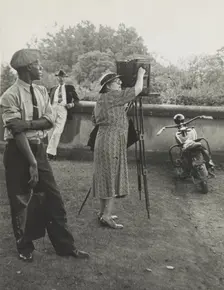 Photographer Frances Benjamin Johnston standing beside her view camera preparing to take..., 1938. Creator: Unknown