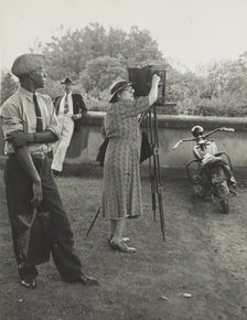 Photographer Frances Benjamin Johnston standing beside her view camera preparing to take..., 1938. Creator: Unknown