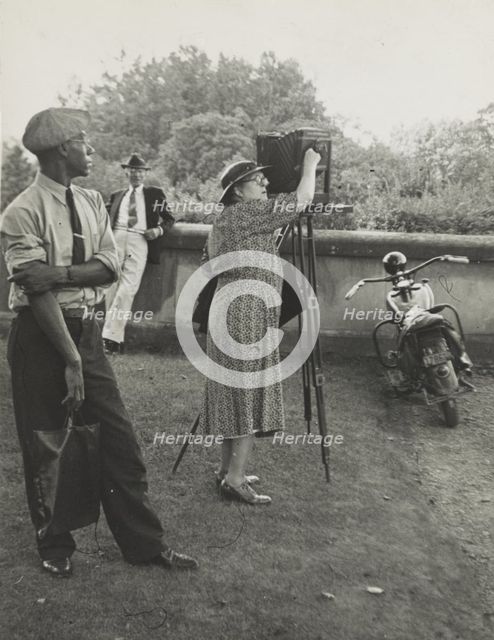 Photographer Frances Benjamin Johnston standing beside her view camera preparing to take..., 1938. Creator: Unknown.