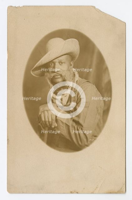 Photographic postcard portrait of a man wearing a hat and overalls, early 20th century. Creator: Unknown.
