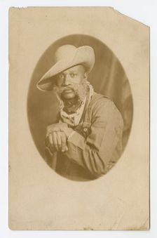 Photographic postcard portrait of a man wearing a hat and overalls, early 20th century. Creator: Unknown