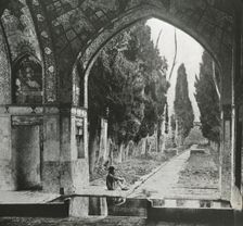 Reproduction of print showing Garden at Fin-Nahe¯, Kashan, Iran. Man seated under arch , c1920. Creator: Frances Benjamin Johnston
