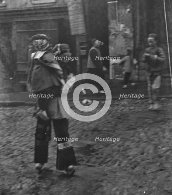 Woman carrying a child crossing a street, Chinatown, San Francisco, between 1896 and 1906. Creator: Arnold Genthe.