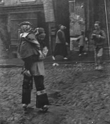 Woman carrying a child crossing a street, Chinatown, San Francisco, between 1896 and 1906. Creator: Arnold Genthe