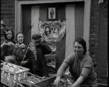 Woman and Others Standing Behind a Street Stall With Wall Behind Decorated With Flags..., 1937. Creator: British Pathe Ltd