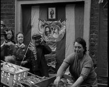 Woman and Others Standing Behind a Street Stall With Wall Behind Decorated With Flags..., 1937. Creator: British Pathe Ltd