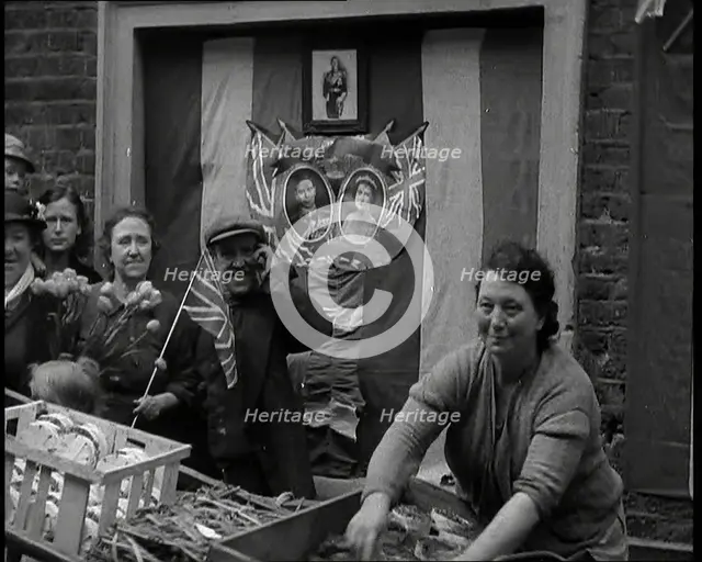 Woman and Others Standing Behind a Street Stall With Wall Behind Decorated With Flags..., 1937. Creator: British Pathe Ltd.