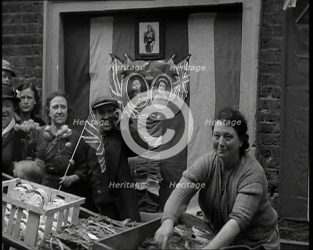 Woman and Others Standing Behind a Street Stall With Wall Behind Decorated With Flags..., 1937. Creator: British Pathe Ltd.