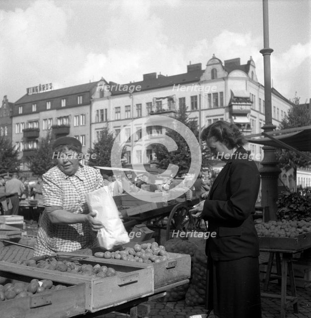 Woman buying potatoes from a fruit and vegetable stall in the market, Malmö, Sweden, 1947. Creator: Otto Ohm.