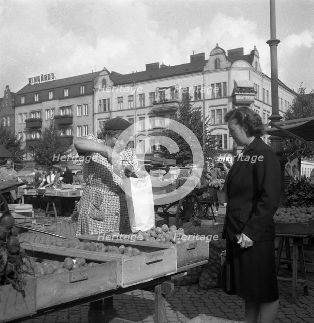Woman buying potatoes from a fruit and vegetable stall in the market, Malmö, Sweden, 1947. Creator: Otto Ohm.