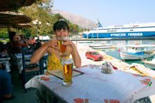 Woman enjoying a drink in a harbourside taverna, Poros, Kefalonia, Greece