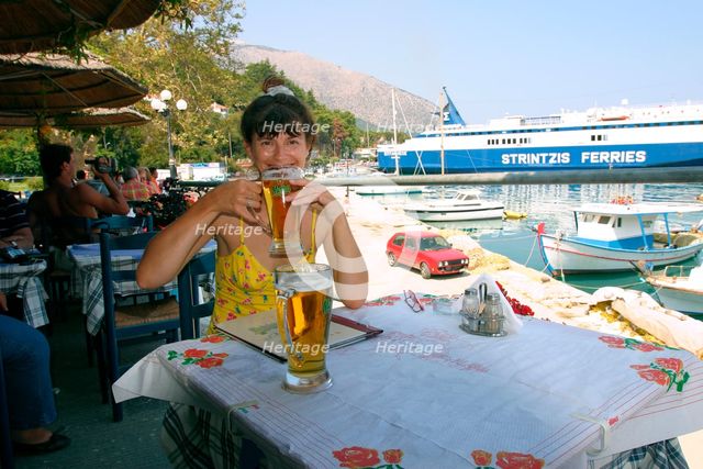 Woman enjoying a drink in a harbourside taverna, Poros, Kefalonia, Greece