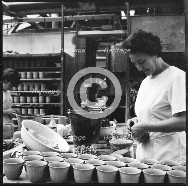 Woman fixing handles to mugs prior to firing in a pottery works, Stoke-on-Trent, 1965-1968. Creator: Eileen Deste.