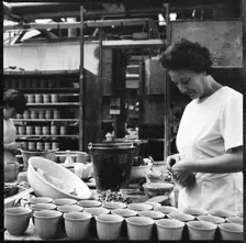 Woman fixing handles to mugs prior to firing in a pottery works, Stoke-on-Trent, 1965-1968. Creator: Eileen Deste