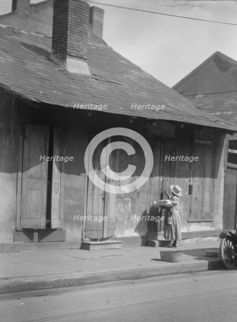Woman holding a sack standing by the doorway of a building in the French Quarter..., c1920-c1926. Creator: Arnold Genthe.
