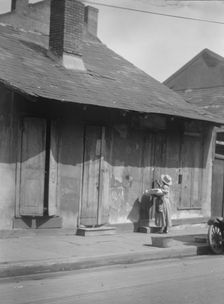 Woman holding a sack standing by the doorway of a building in the French Quarter..., c1920-c1926. Creator: Arnold Genthe