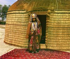 Woman in traditional dress and jewelry standing on rug in front of yurt, between 1905 and 1915. Creator: Sergey Mikhaylovich Prokudin-Gorsky