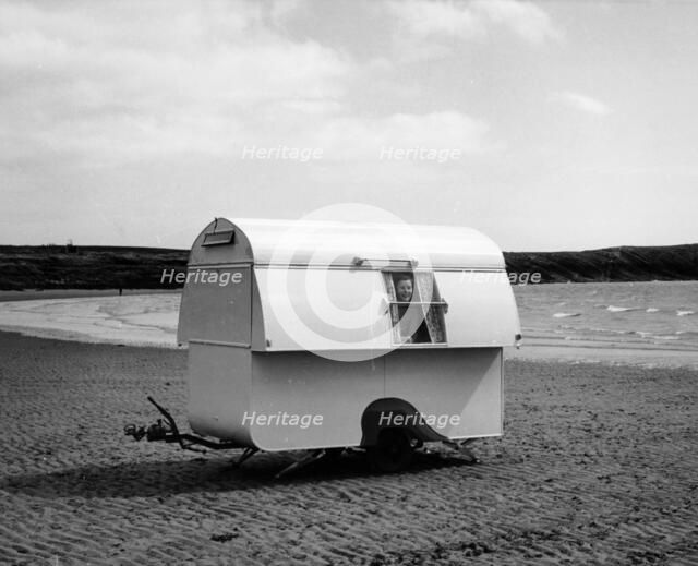 Woman smiling from the window of a trailer caravan on a beach, (c1960s?). Artist: Unknown