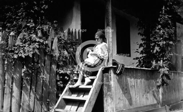 Woman sewing on her porch steps, Bistrita Valley, Moldavia, north-east Romania, c1920-c1945. Artist: Adolph Chevalier