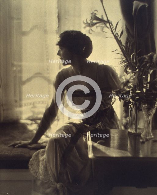 Woman sitting on window seat, looking left, full-length portrait, between 1900 and 1920. Creator: Unknown.