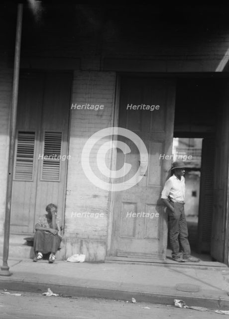 Woman sitting on steps and man standing in a doorway, New Orleans, between 1920 and 1926. Creator: Arnold Genthe.