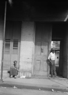 Woman sitting on steps and man standing in a doorway, New Orleans, between 1920 and 1926. Creator: Arnold Genthe