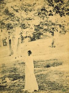 Woman standing in a park, trees in background, c1900. Creator: Eva Watson-Schutze