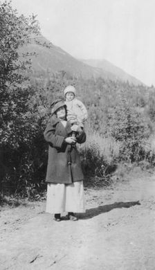 Woman standing on dirt road holding child; mountains in background, between c1900 and 1916. Creator: Unknown