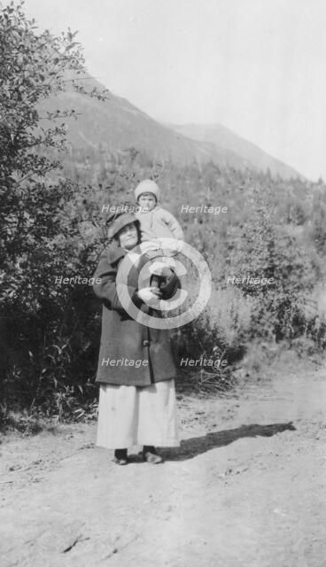 Woman standing on dirt road holding child; mountains in background, between c1900 and 1916. Creator: Unknown.
