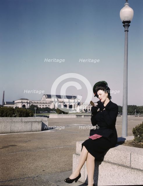 Woman putting on her lipstick in a park with Union Station behind her, Washington, D.C., ca. 1943. Creator: Unknown.