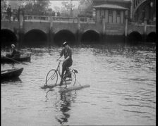 Woman Riding Along a River on a Floating Bicycle Contraption, 1920. Creator: British Pathe Ltd