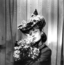 Woman wearing a hat with a veil, holding a bouquet of flowers, Paris, 1943